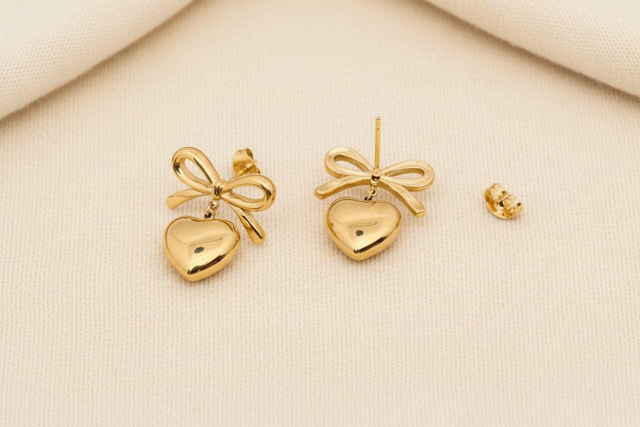 front and back view of a pair of gold bow and heart earrings laying on grey carpet