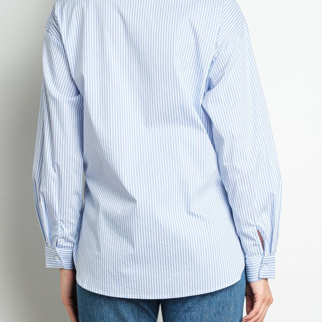Back view of a woman wearing blue and white striped rhinestone blouse with sequin flower details. Back side does not have any embellishment