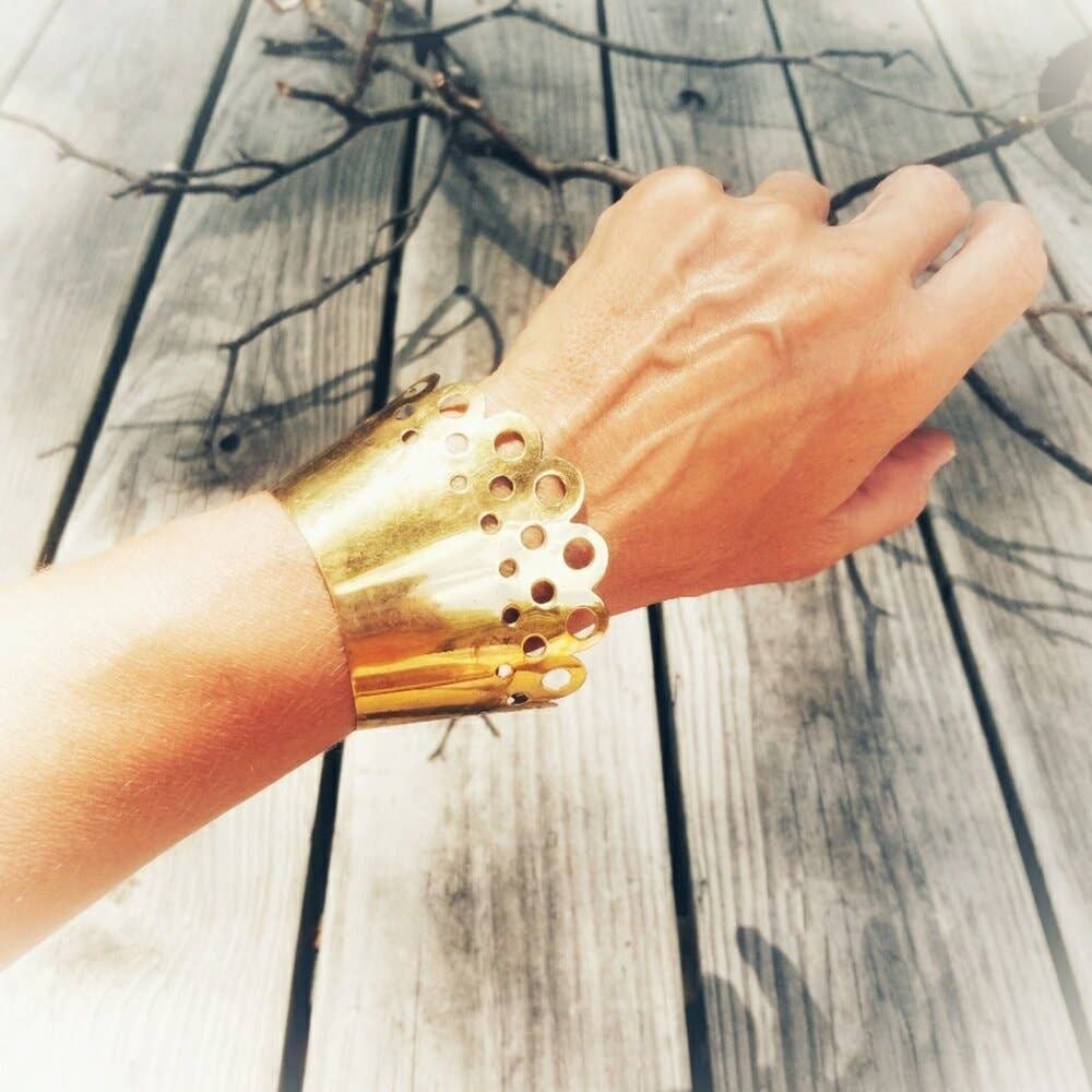 Brass Scallop cuff on an arm in front of wood and branches