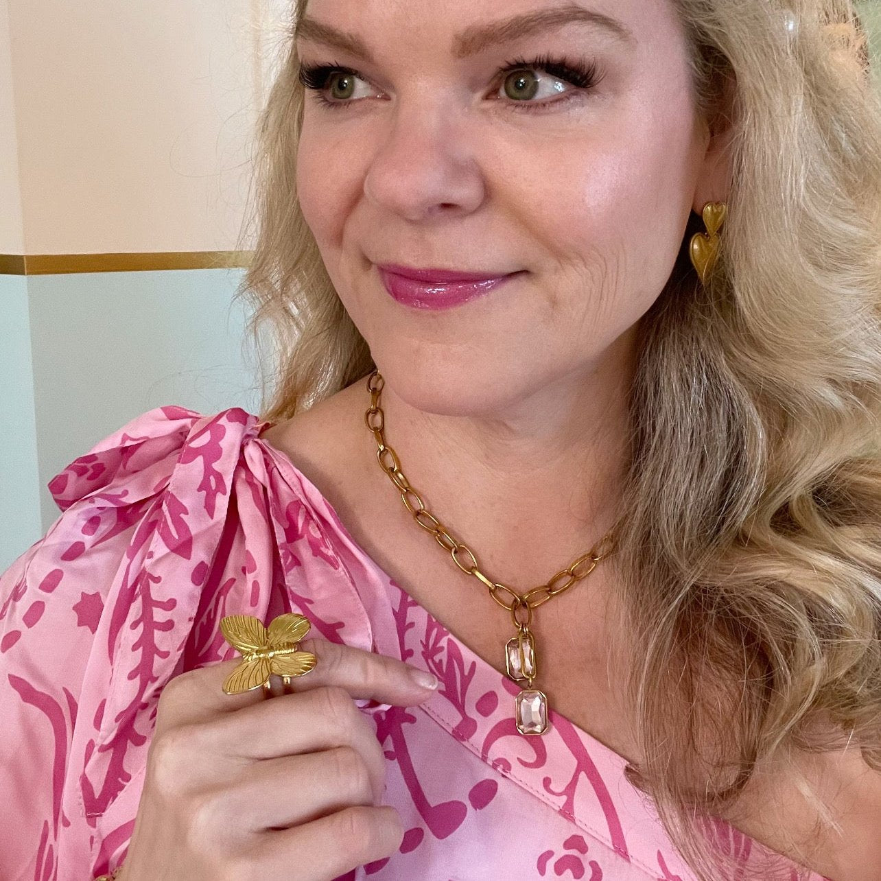 woman in pink dress wearing gold butterfly cocktail ring and gold pendant necklace