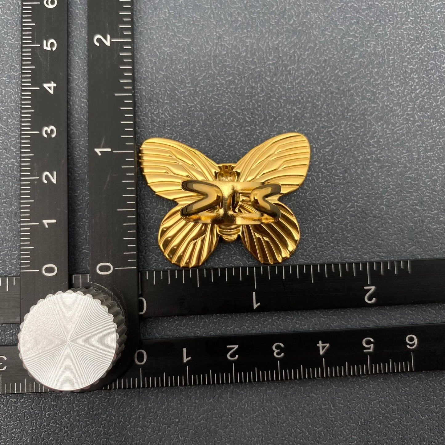 the back of a gold butterfly cocktail ring next to a ruler