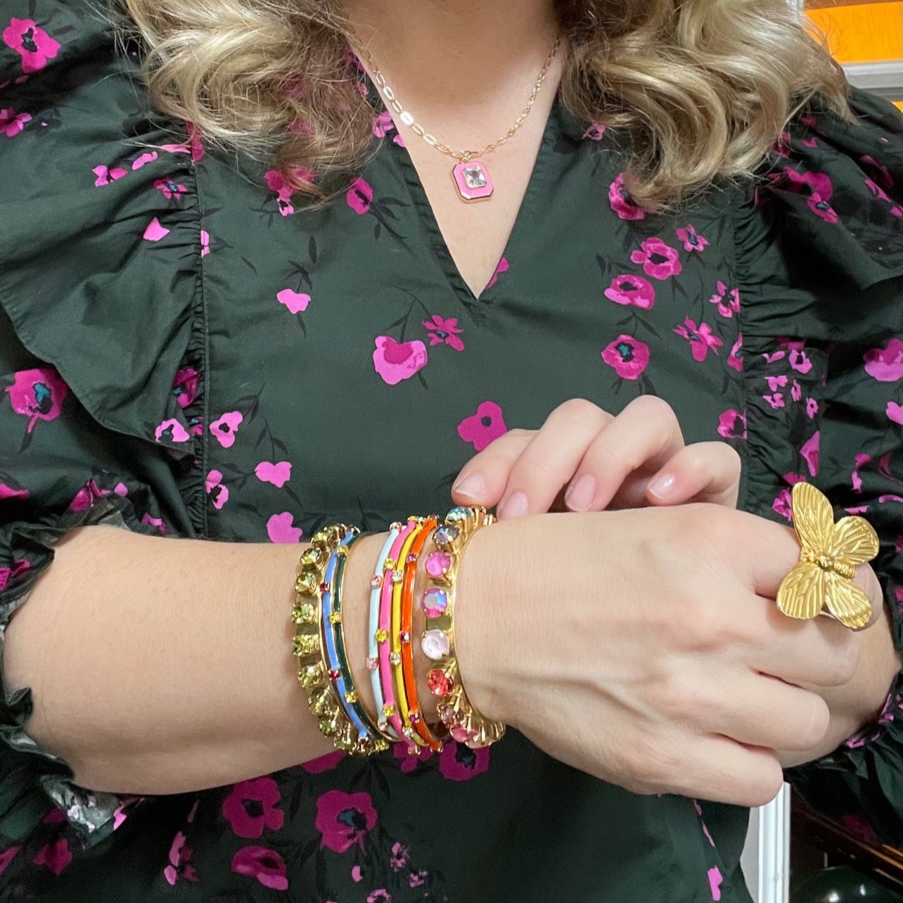 woman in green and pink blouse and gold butterfly ring wearing multiple enamel bracelets with crystals
