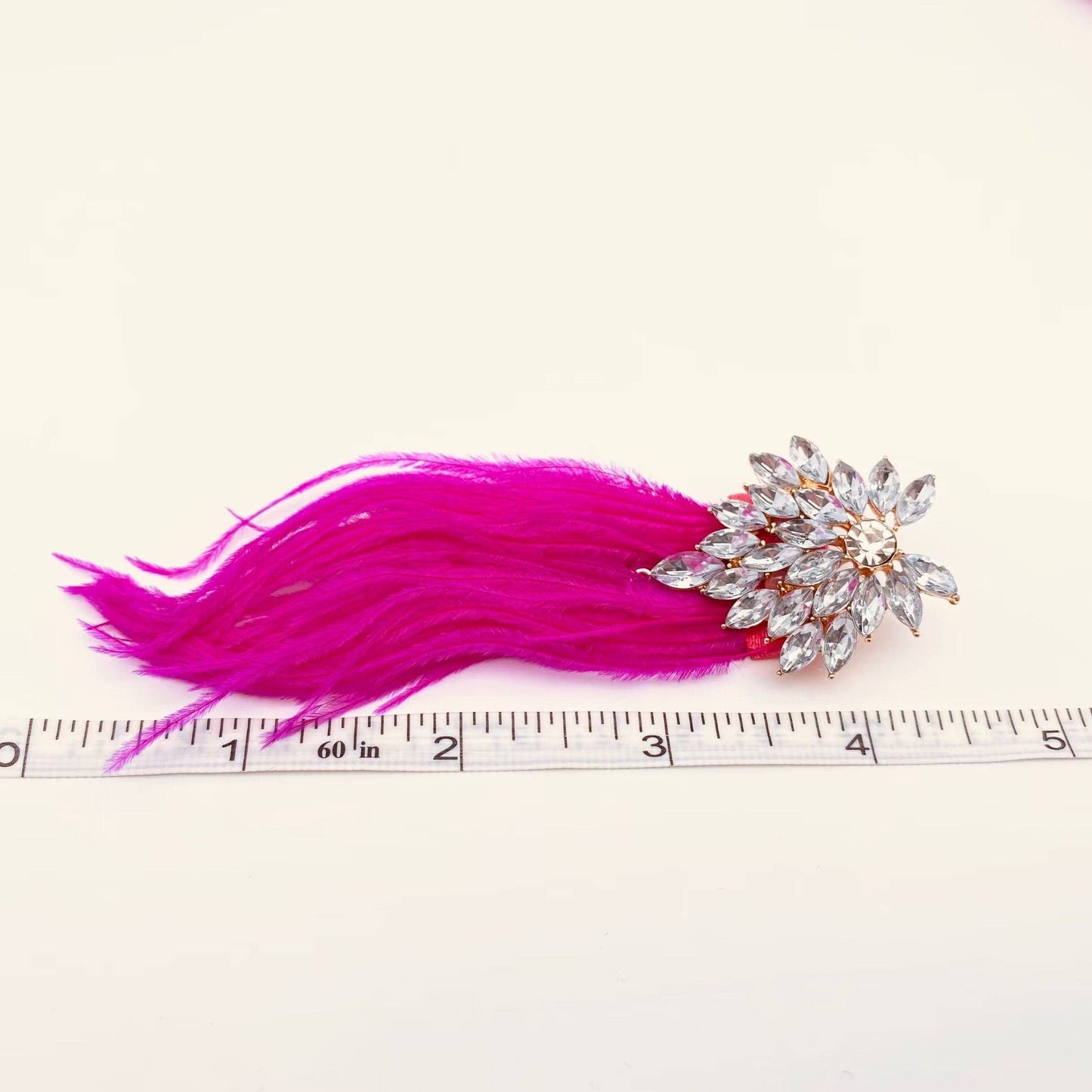 one pink feather and rhinestone encrusted earring next to a ruler