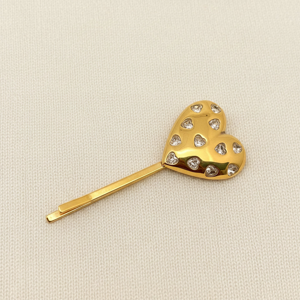 A gold heart hair pin with inlaid rhinestones against an ivory background