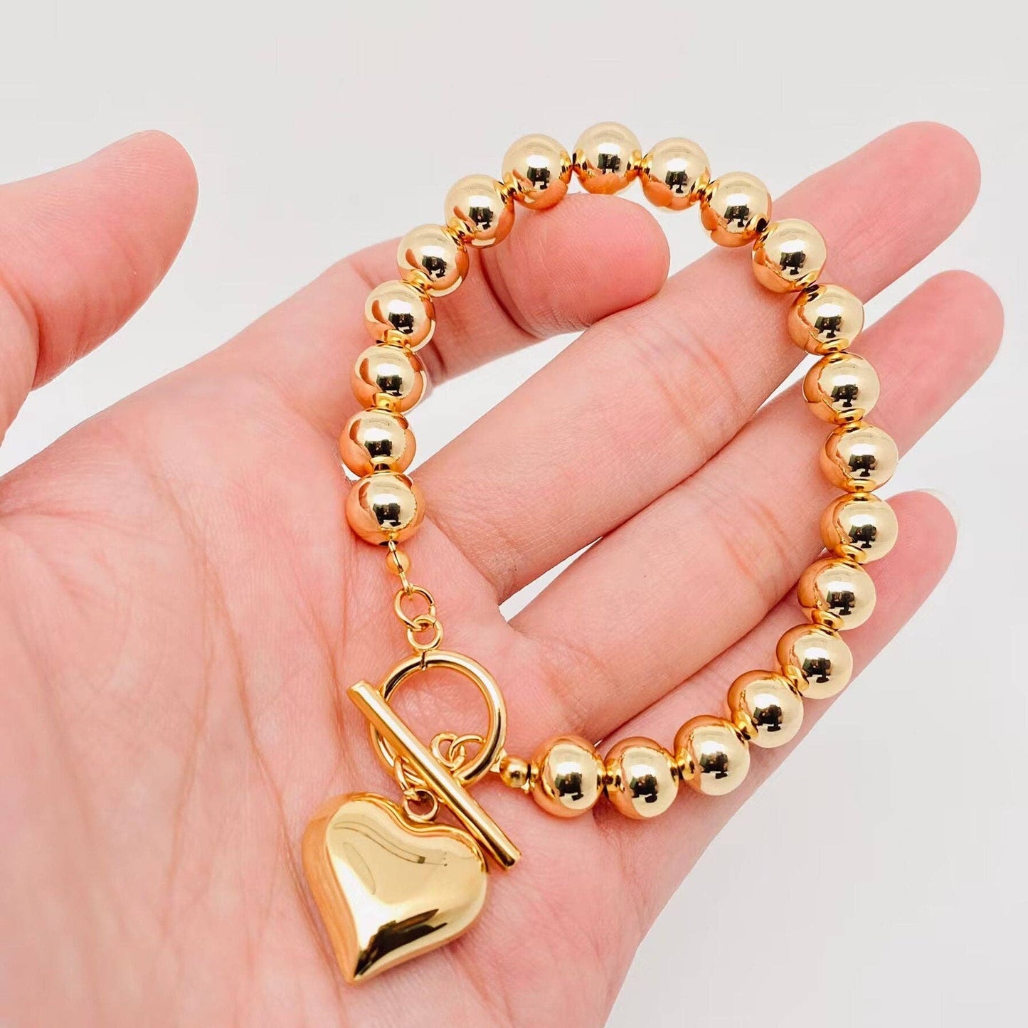 gold bead bracelet with puffy heart charm and toggle clasp in hand