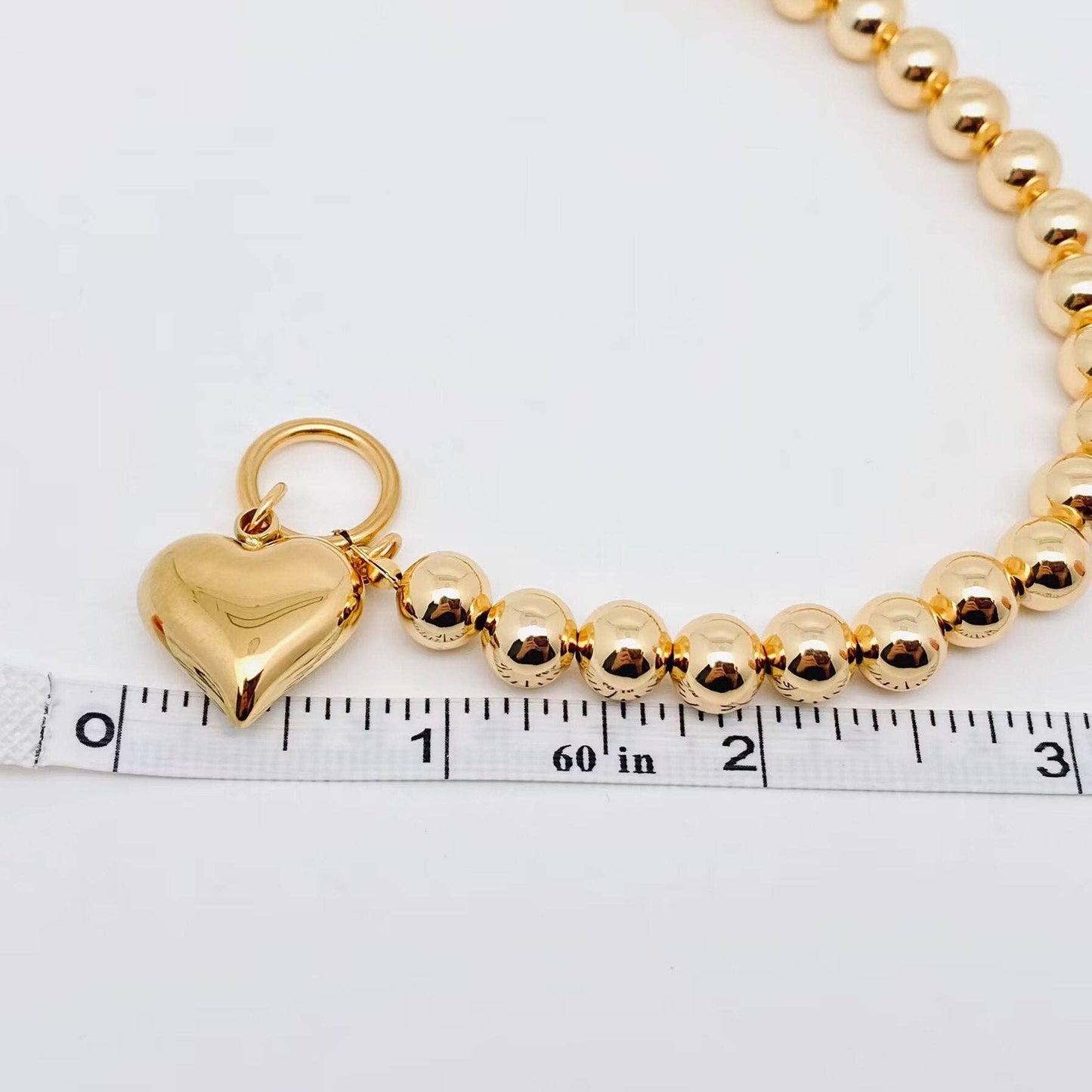 gold bead bracelet with puffy heart charm and toggle clasp next to ruler to show scale