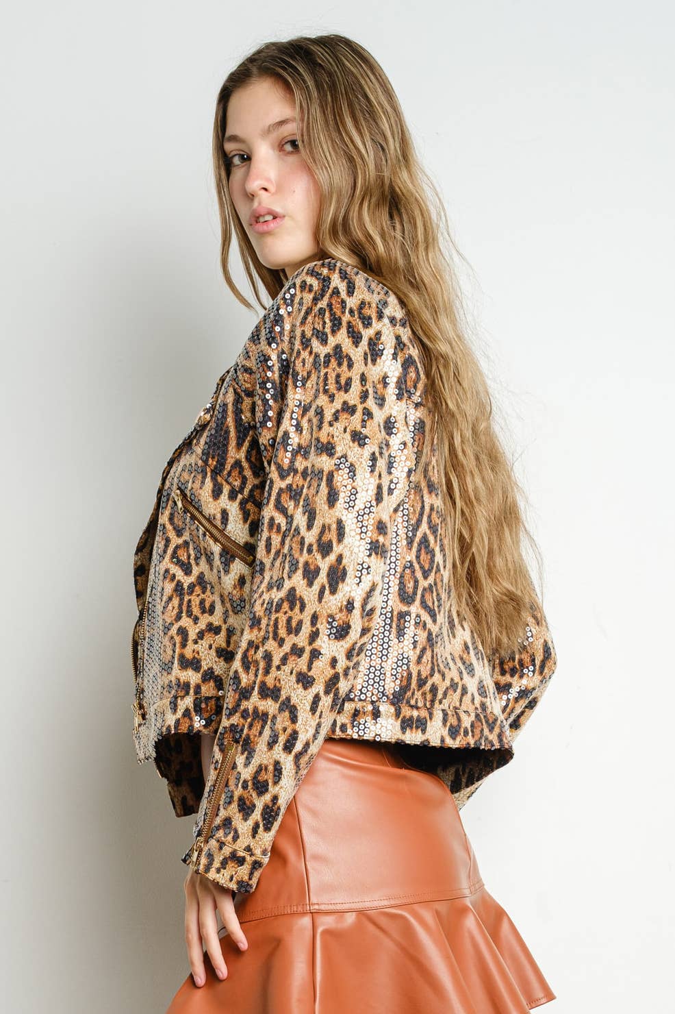 Side view of woman wearing a sequined leopard print moto jacket with zipper detail on sleeves against a white background