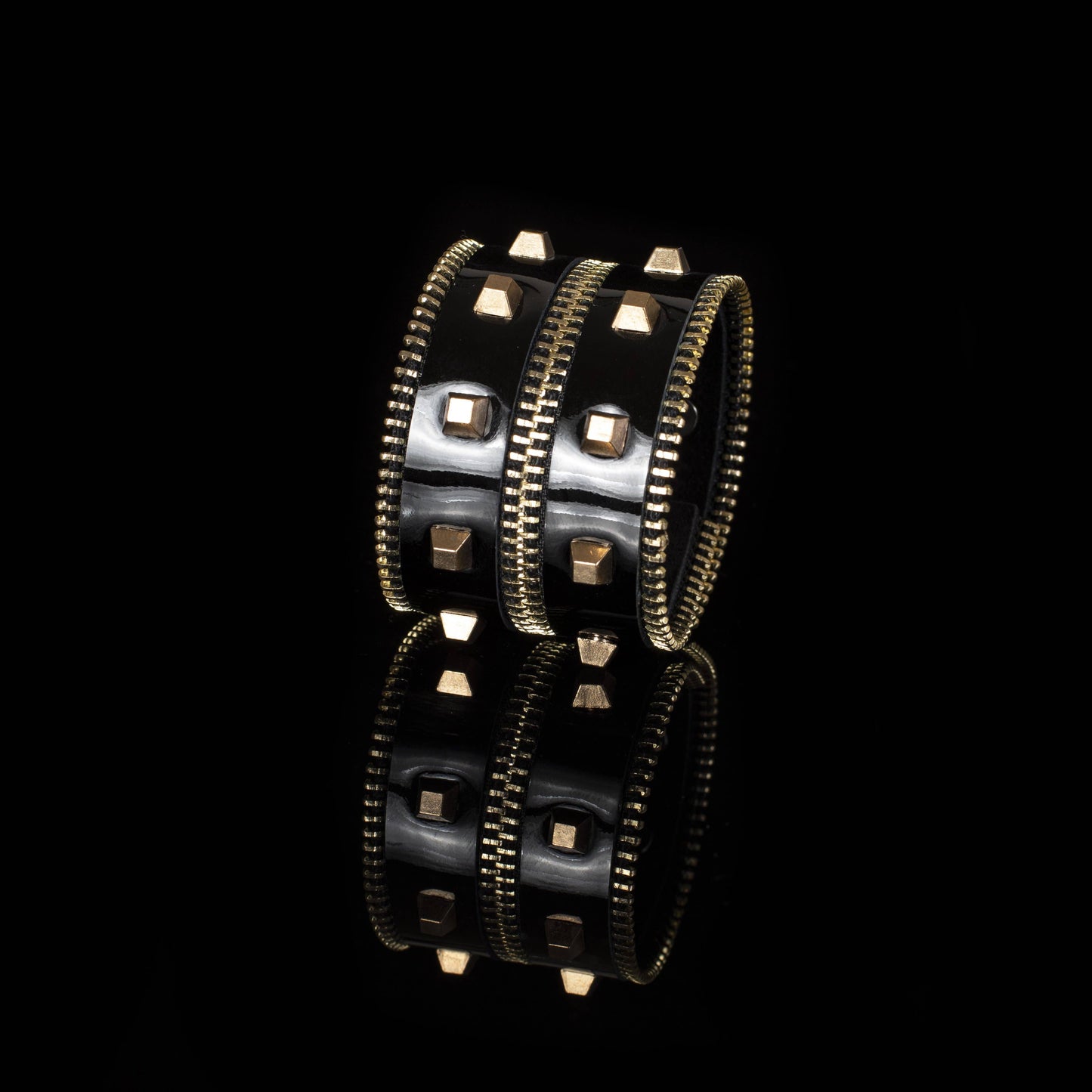 black leather cuff bracelet with gold studded detailing against a black background