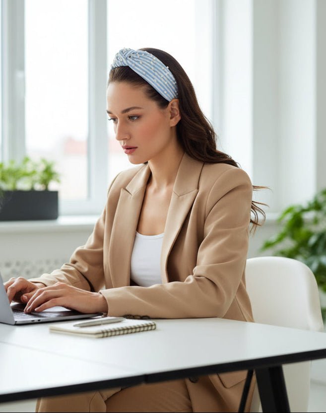 Woman wearing a light blue and white striped heaband pearl embellishment, sitting at a computer in a work environment