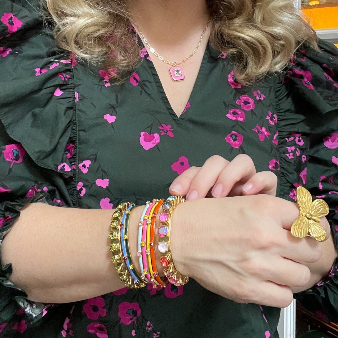 woman in green and pink floral blouse with gold butterfly ring and multiple gold and crystal bracelets