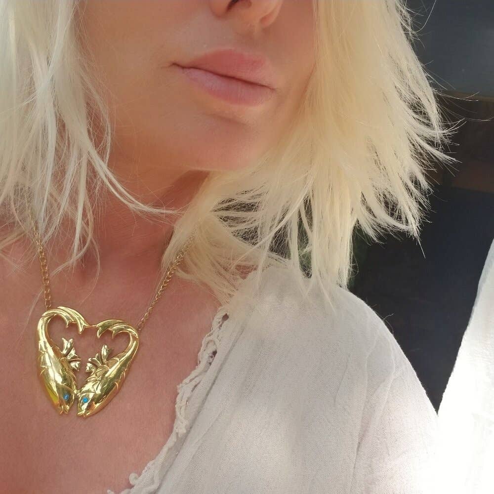 woman wearing gold double fish shaped necklace with aquamarine inlaid stones