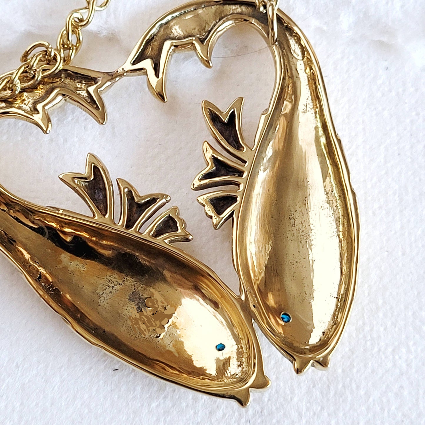 back view of double fish shaped gold necklace with aquamarine inlaid stones for the eyes