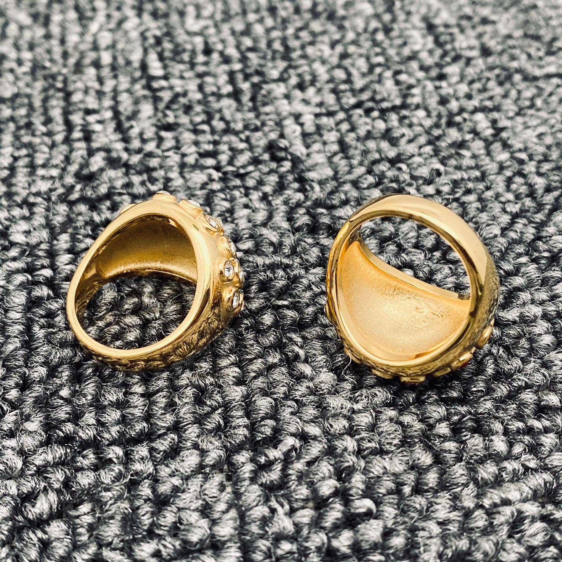 Two gold rings laying a grey carpet to show the side and underside view of the rings.