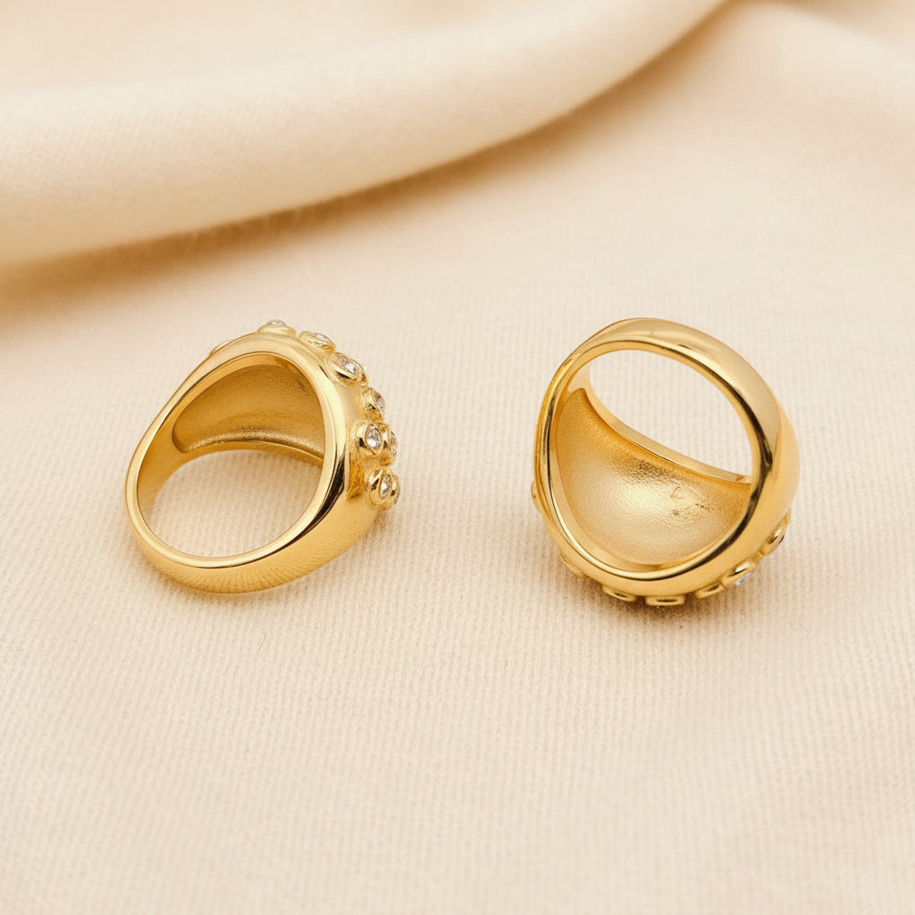 Two gold rings laying an ivory fabric to show the side and underside view of the rings.