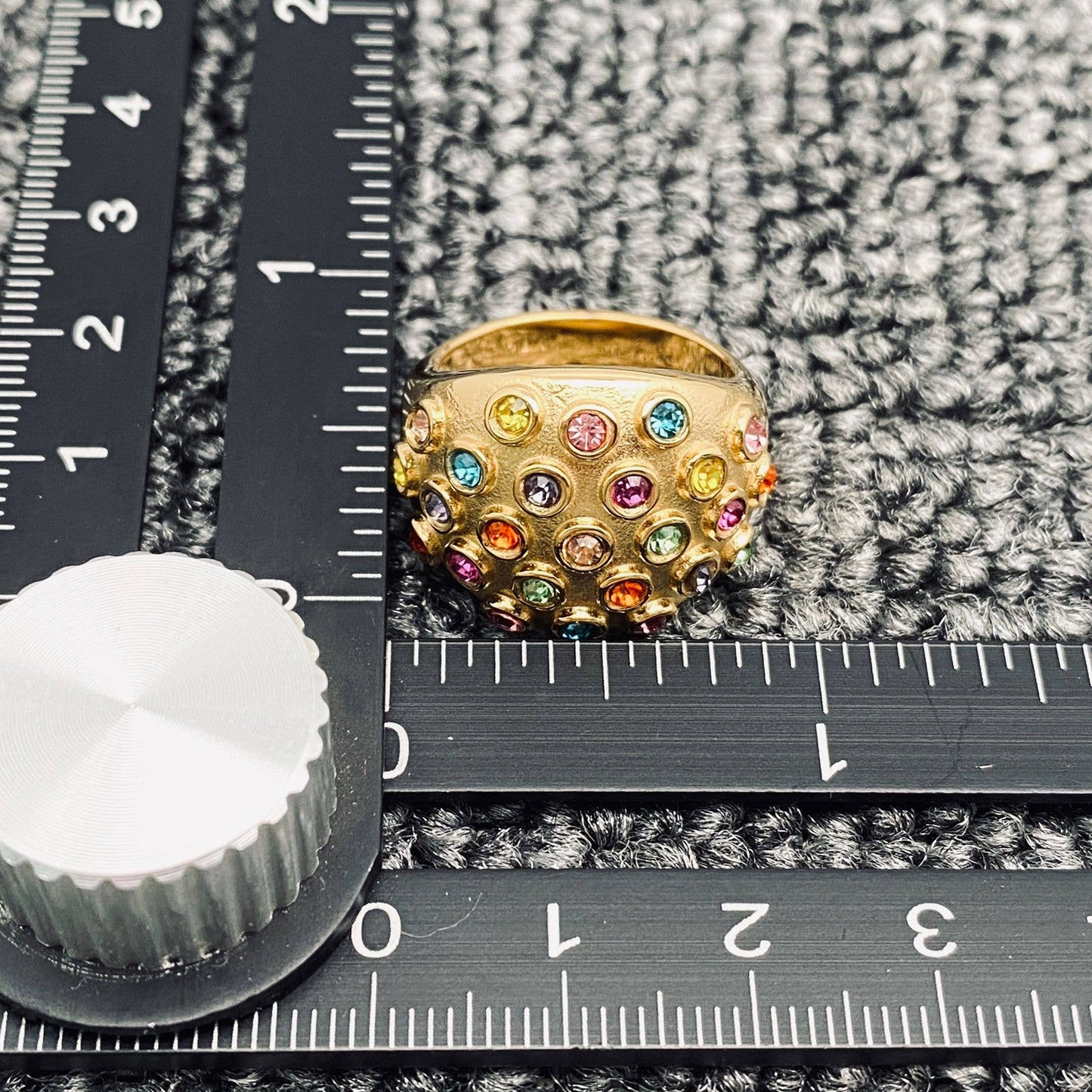 a gold statement ring with multi colored round stones against a black ruler laying on grey carpet