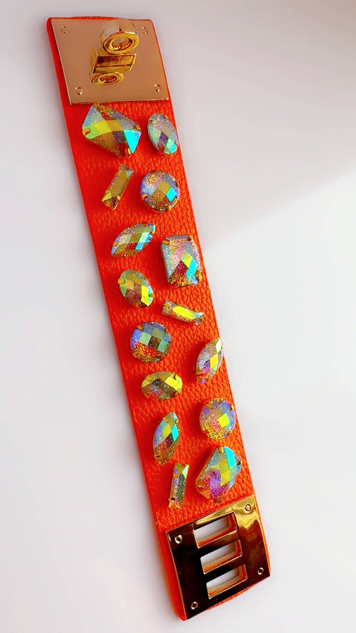Orange leather cuff bracelet with colorful rhinestones laying flat on a white surface with a bird's eye view