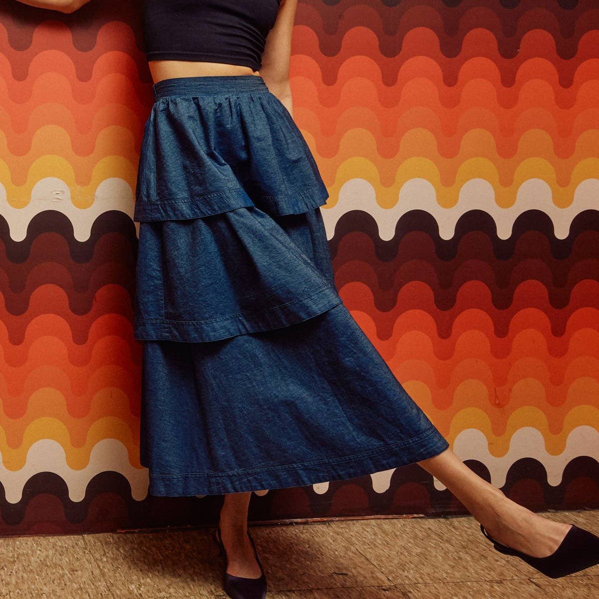 woman in black heels wearing denim tiered midi skirt in front of geometric wall
