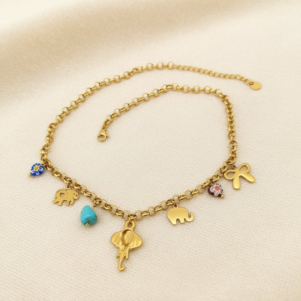 back view of gold multi charm necklace with elephants, bow, and turquoise charms laying on a grey background