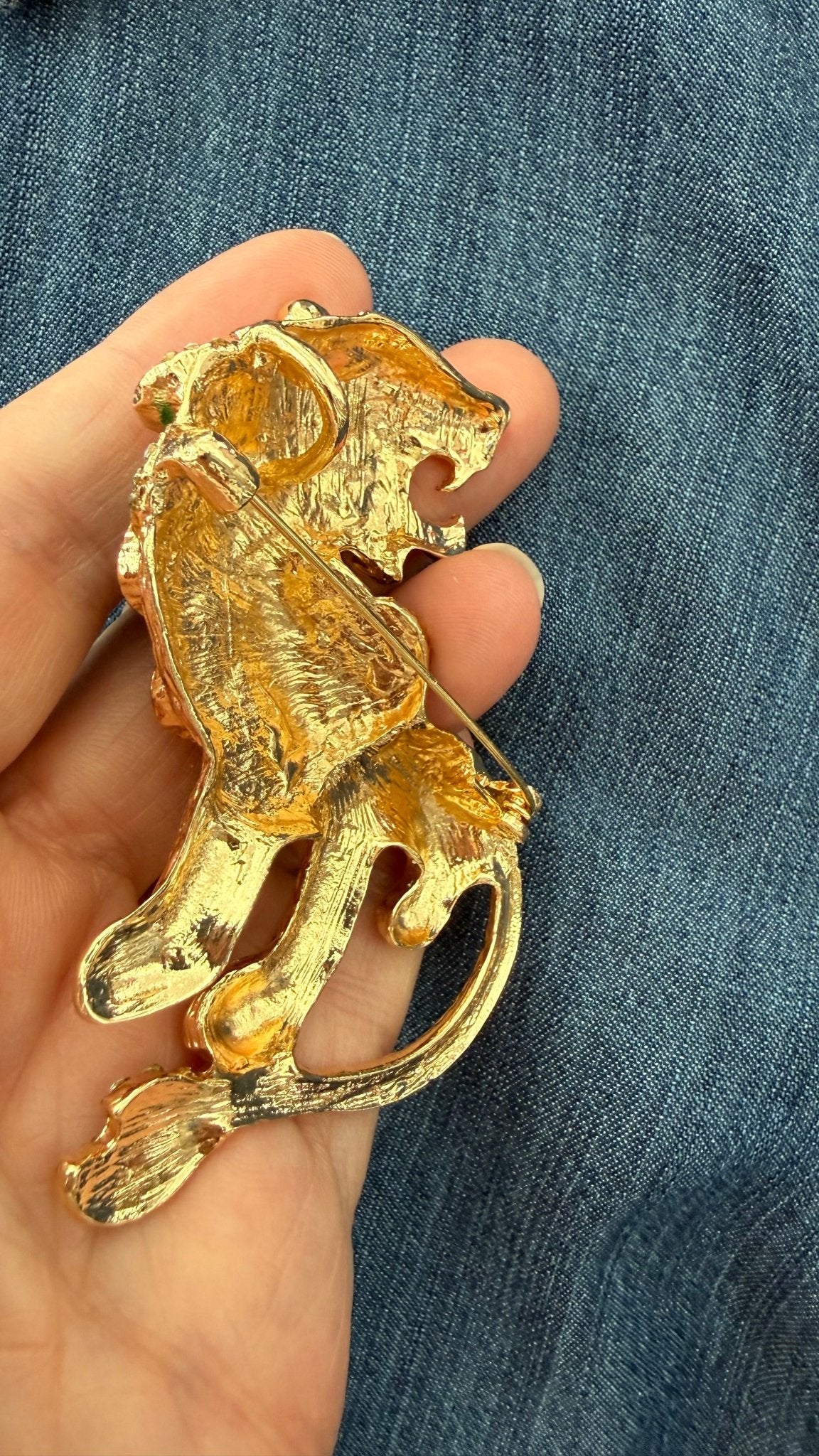 back view of gold lion brooch to show pin closure and round pendant loop against denim fabric
