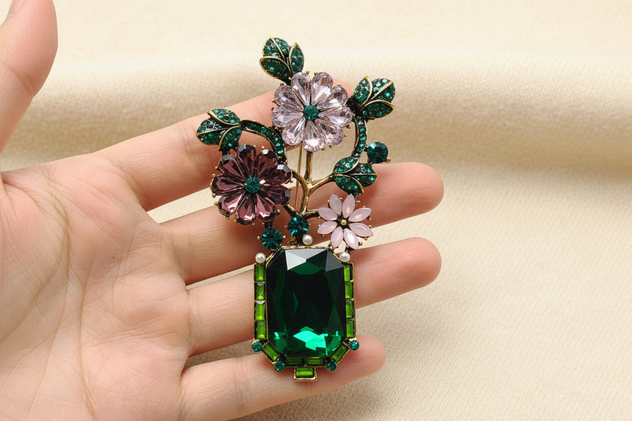 Decorative brooch with floral and gemstone design held in a hand against a gray background