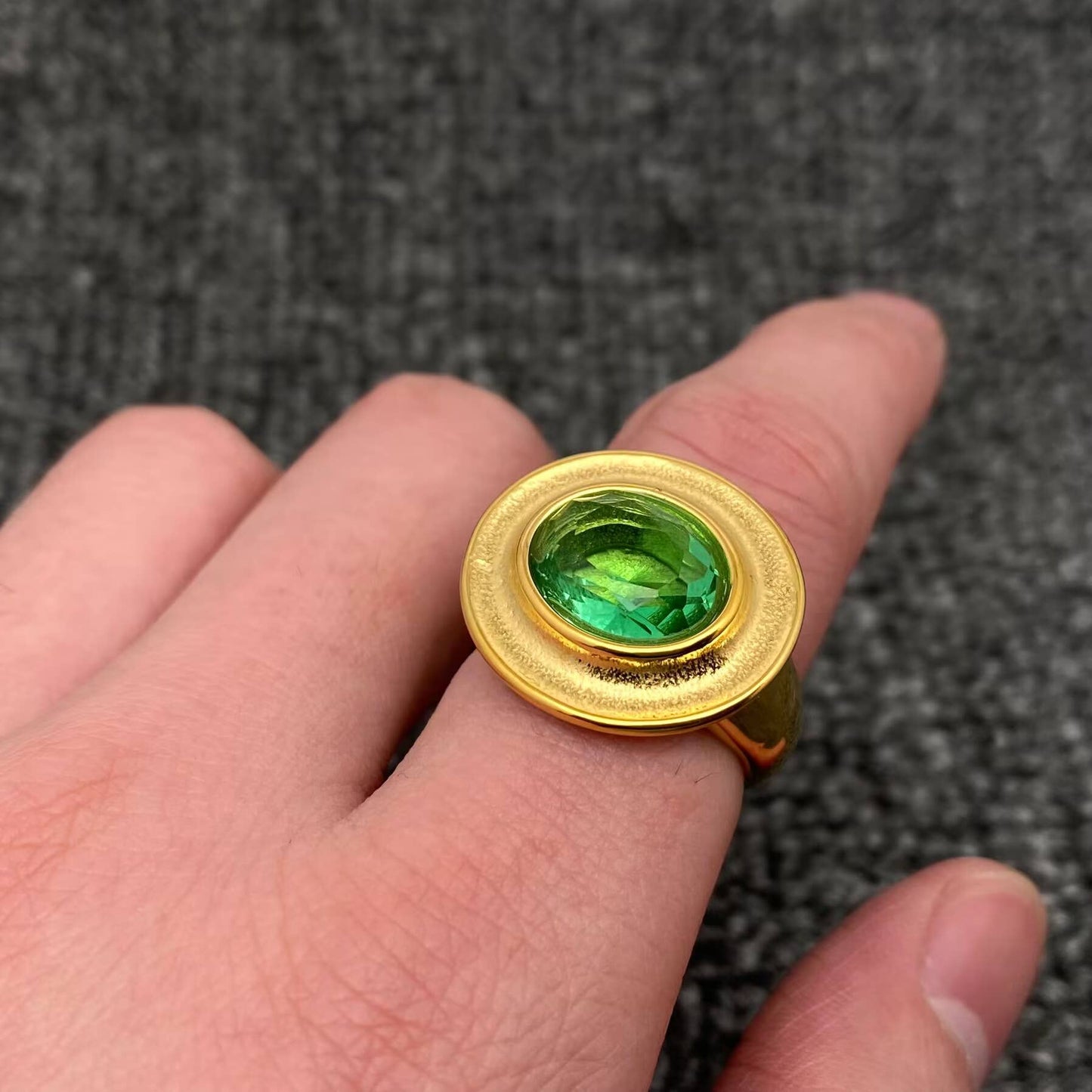 a finger wearing a gold ring with oval green cubic zirconia stone