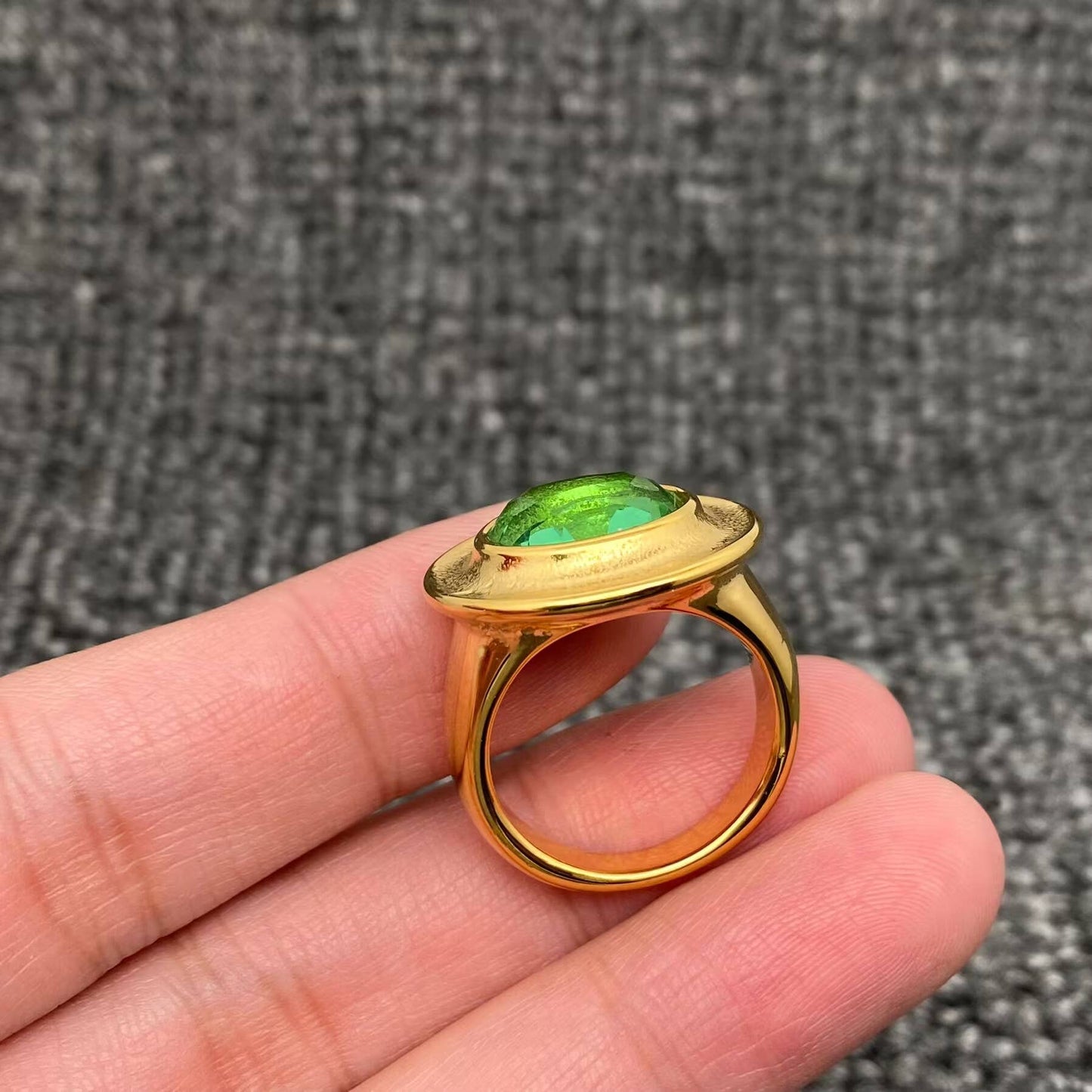 side view of a gold ring with oval green cubic zirconia stone held by 3 fingers
