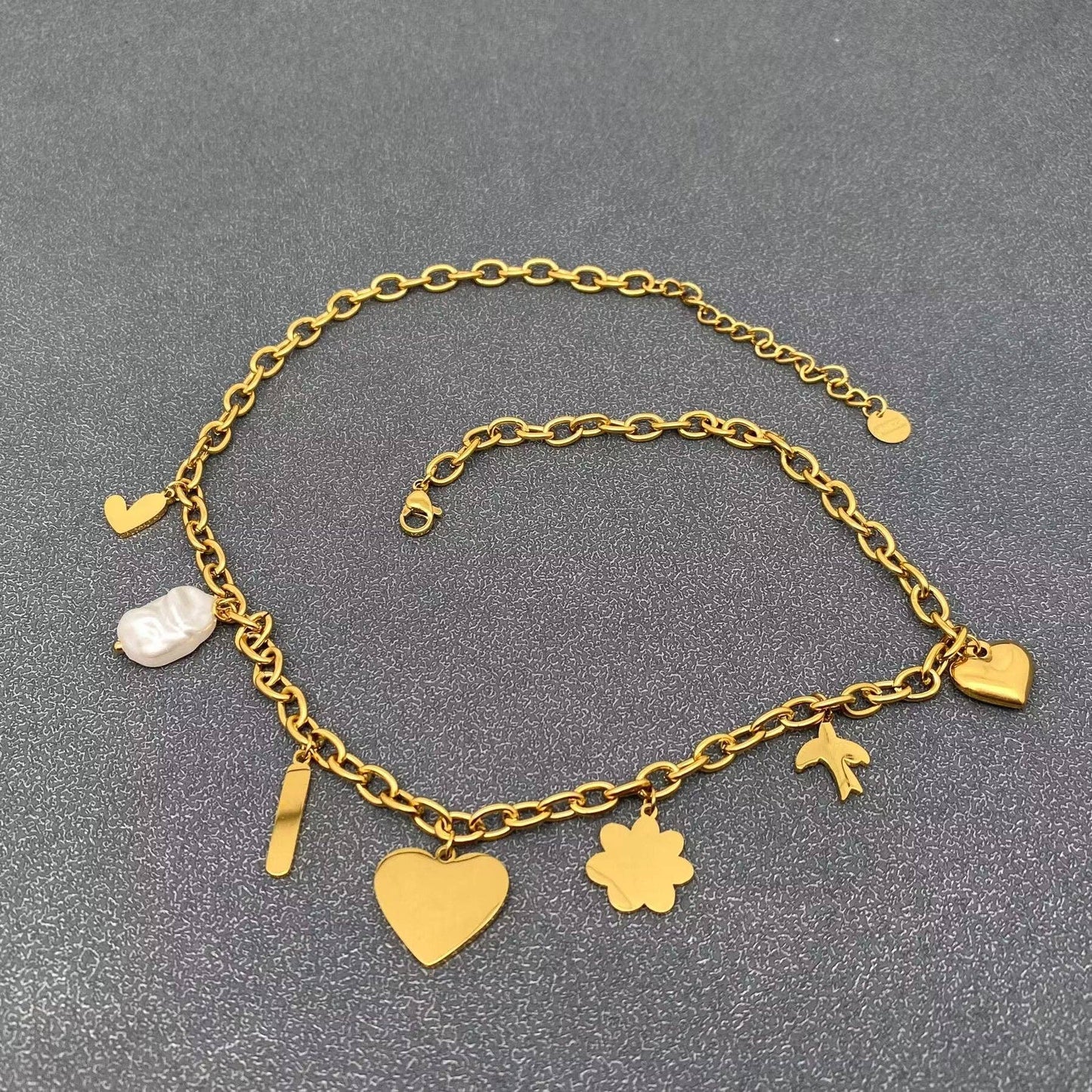 back view of enamel heart multi-charm necklace with seven gold charms on gold link chain against a grey background