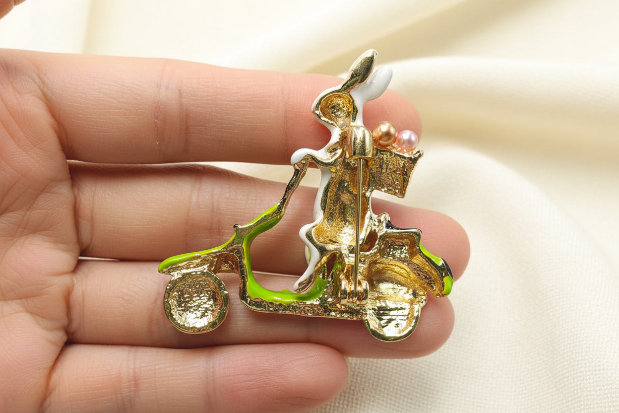 Back view of rabbit on a scooter brooch to show pin closure in a hand against a gray background
