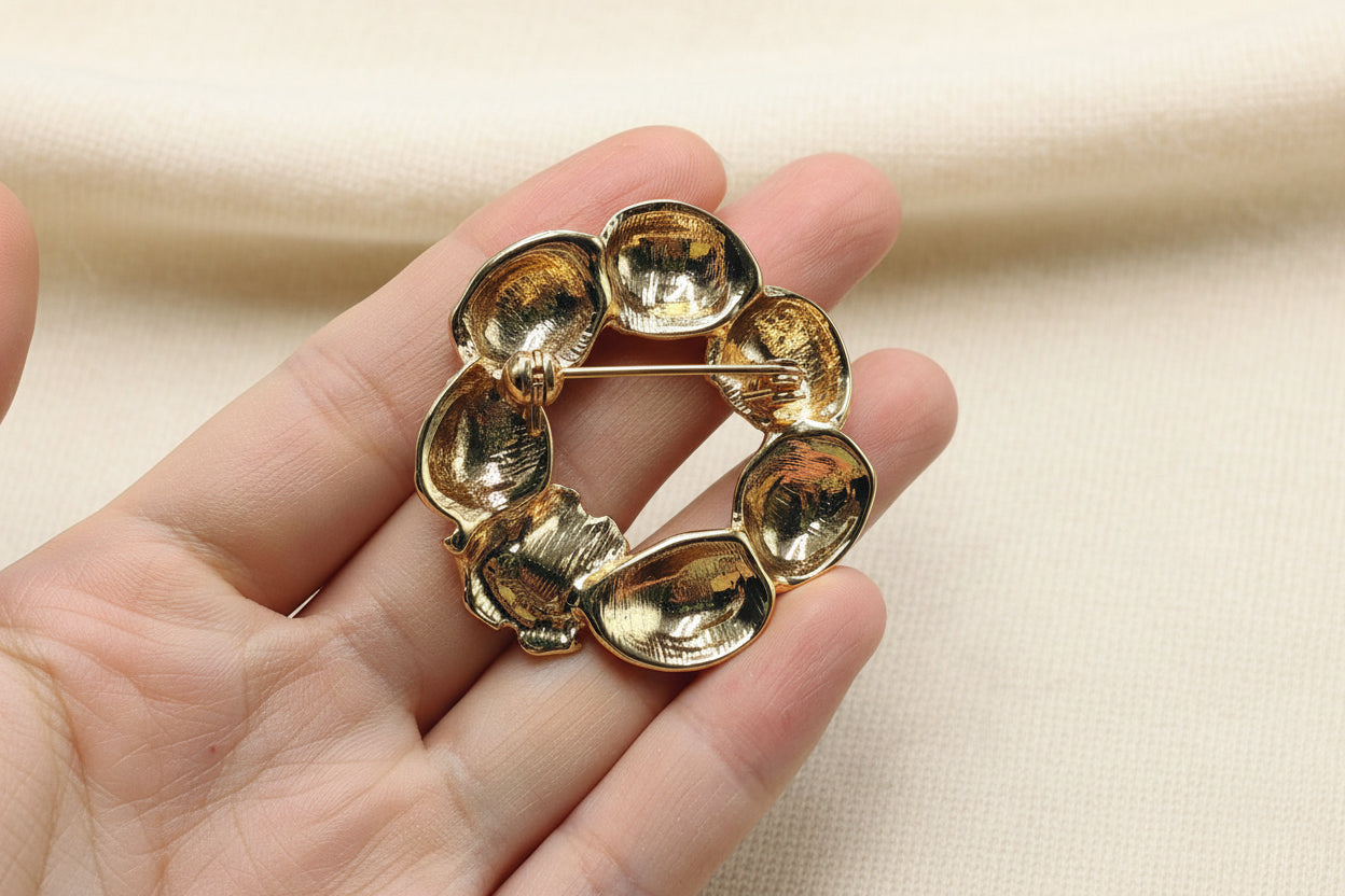 back view of strawberry brooch held in a hand against a gray background