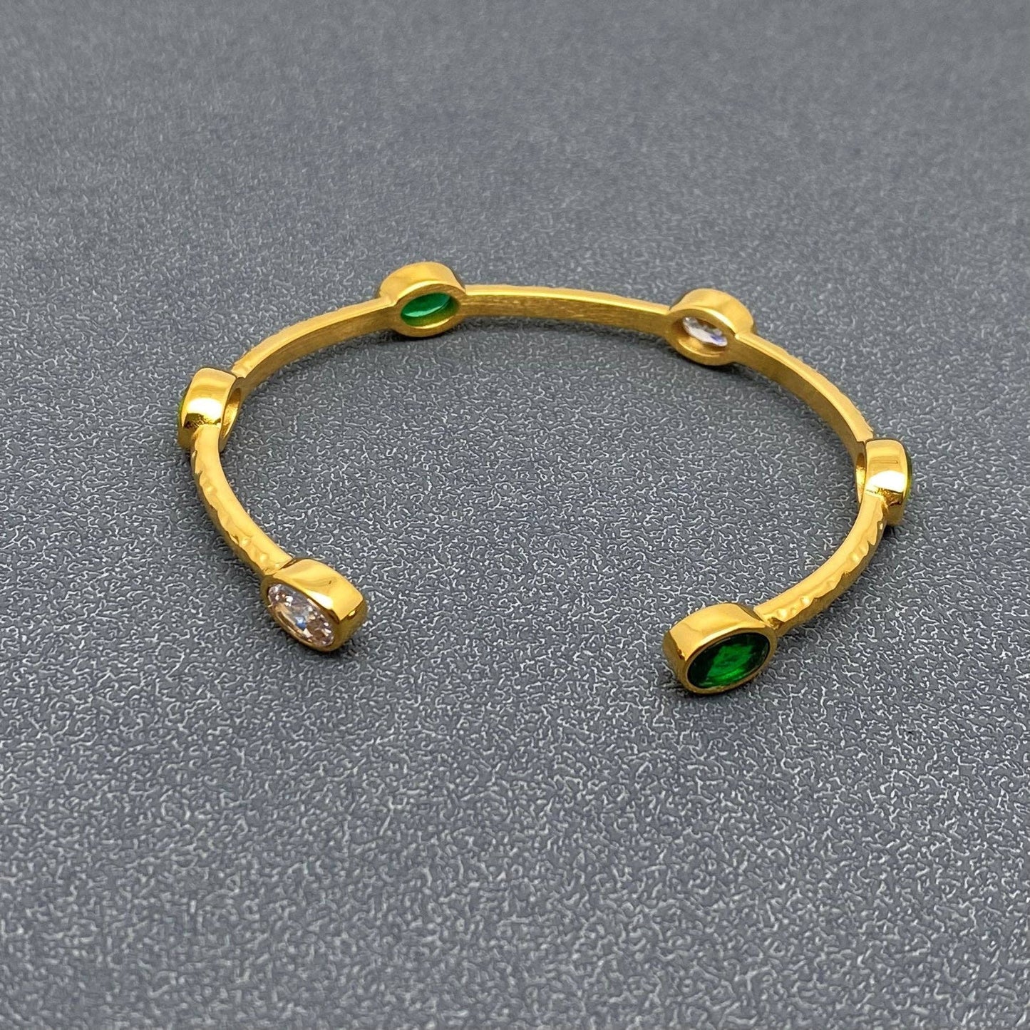 side view of gold adjustable bangle with clear and green colored inlaid crystal stones