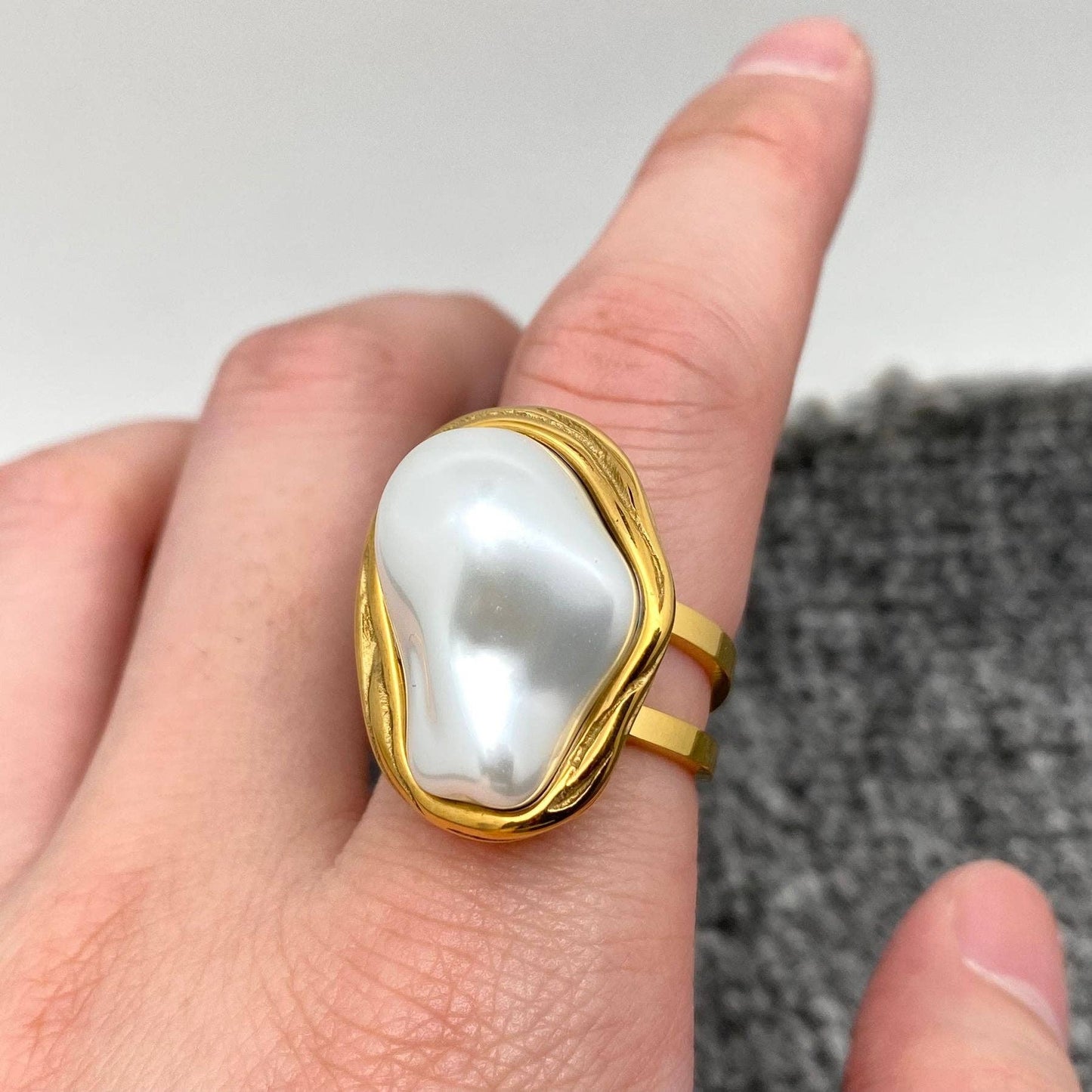 an adjustable gold ring with inlaid white baroque pearl on a finger
