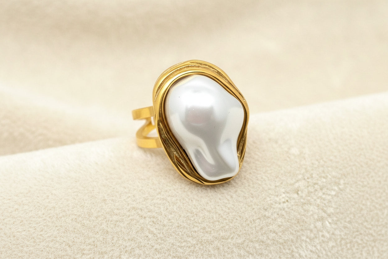 a gold adjustable ring with white baroque style pearl laying on an ivory background