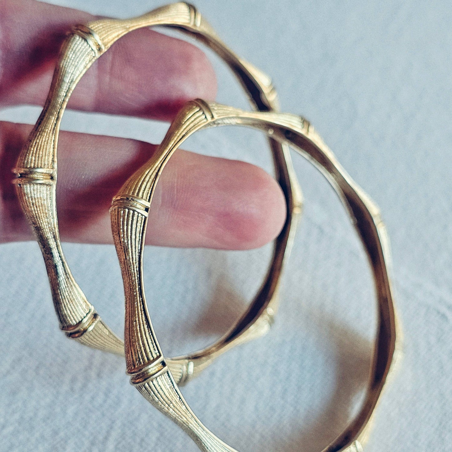 two fingers holding a pair of brass bamboo shaped bangle bracelets