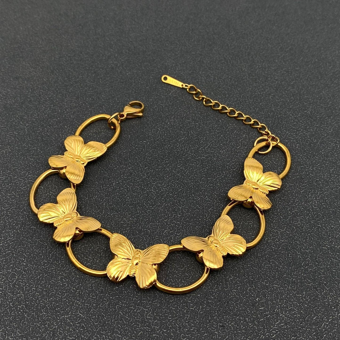 flat view of gold butterfly link bracelet against a grey background