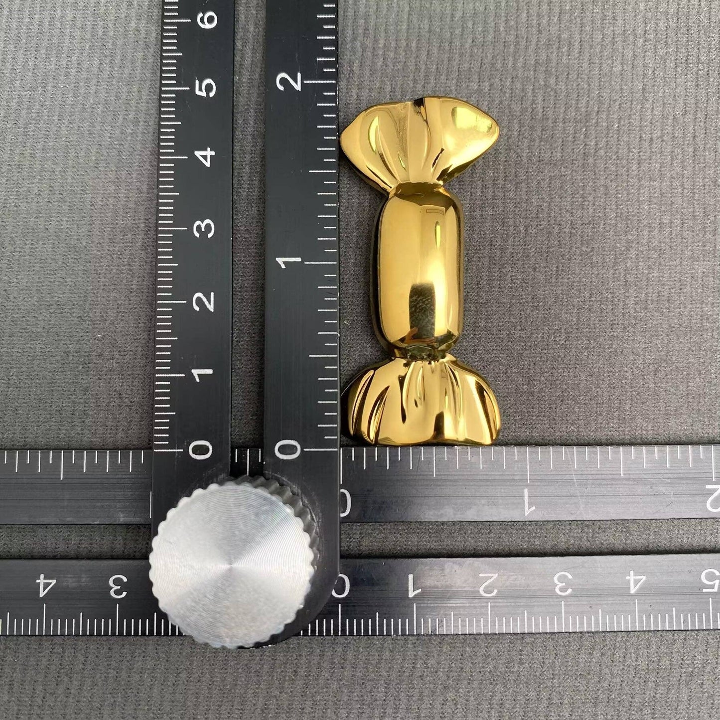 Gold candy wrapper-shaped brooch next to a ruler on a gray background