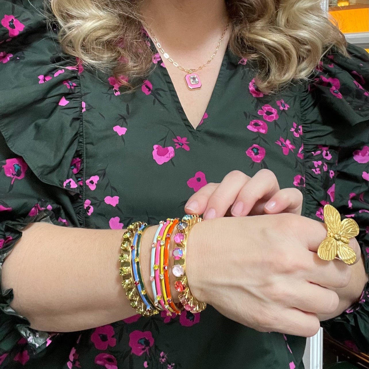 woman in floral blouse wearing gold cuff bracelets in various sizes and a gold butterfly ring
