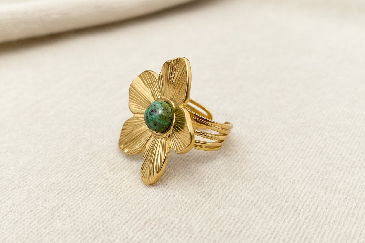 side view of gold flower shaped cocktail ring with green center stone laying on an ivory surface