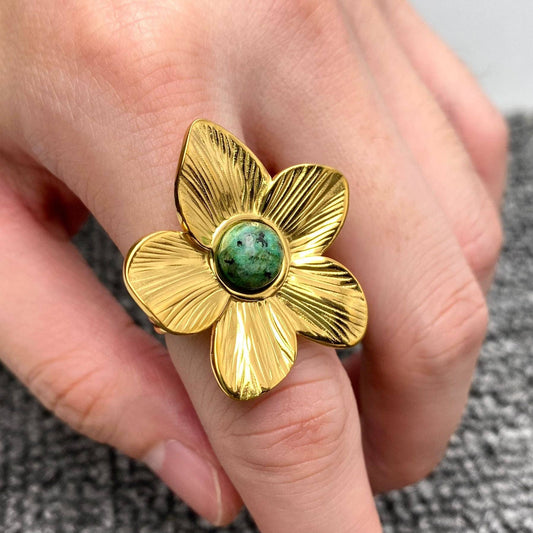 gold flower shaped cocktail ring with center green stone on hand
