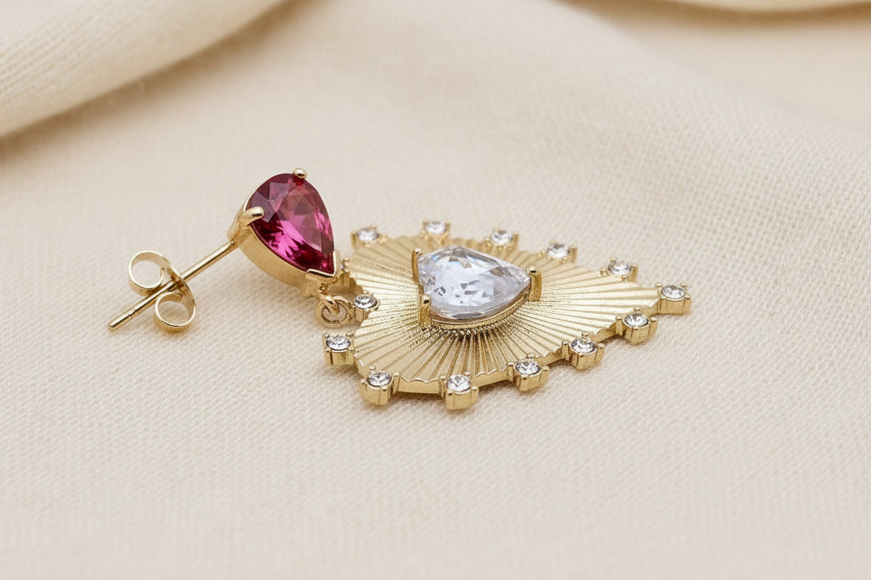 side view of one gold heart earring with red and clear crystals against an ivory background