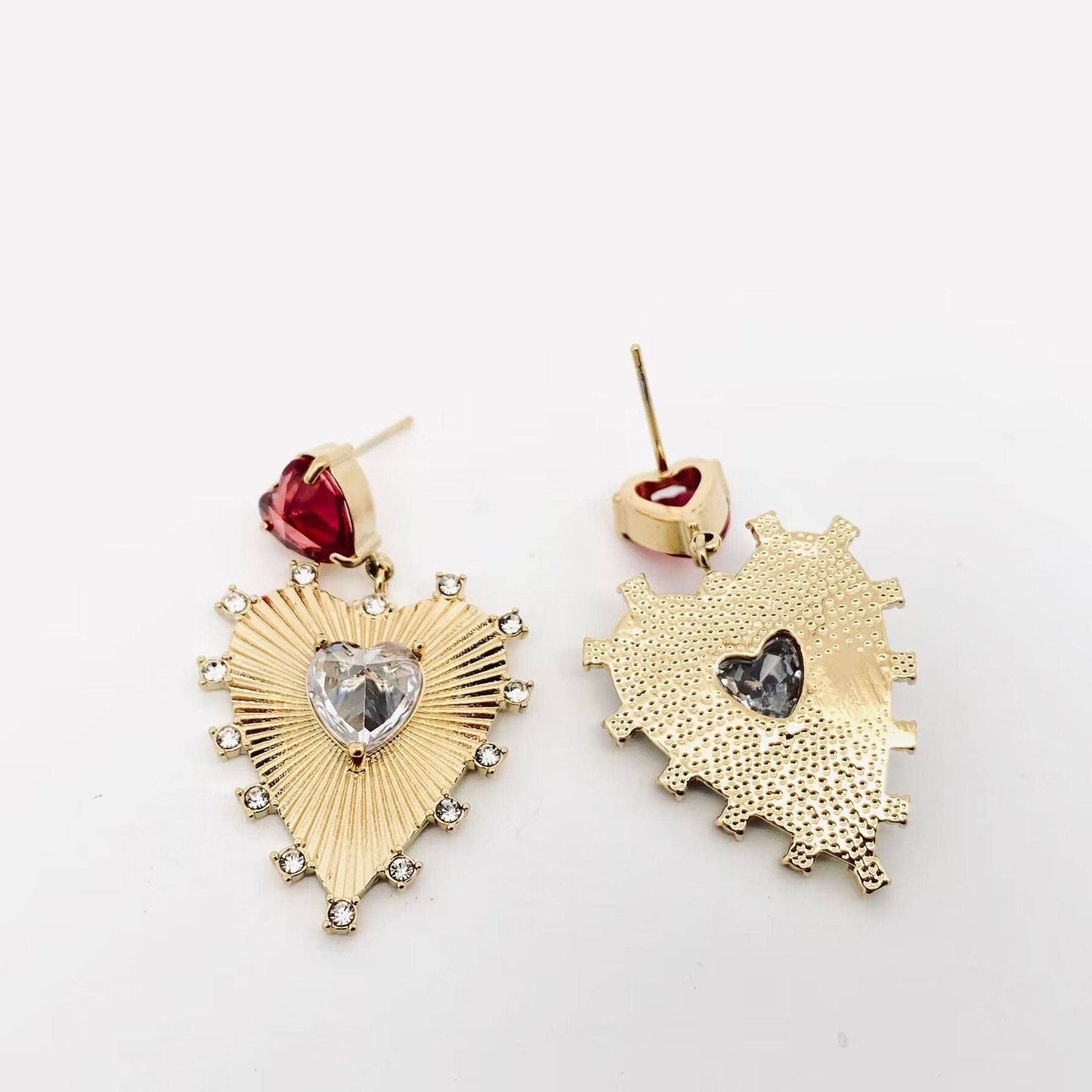 front and back view of gold heart dangle earrings with red and clear stones laying on a white background