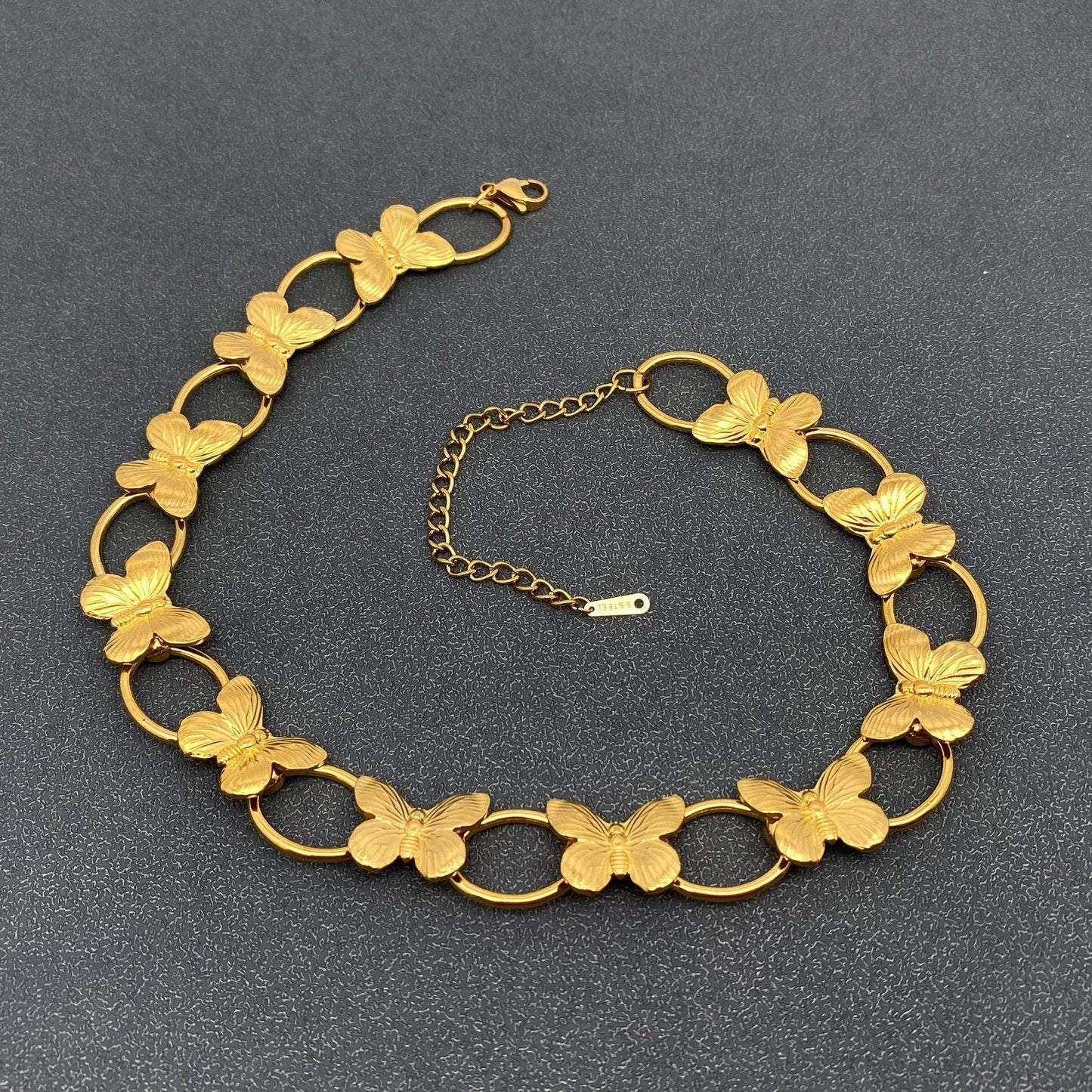 gold necklace with butterflies and circle links laying on a grey background