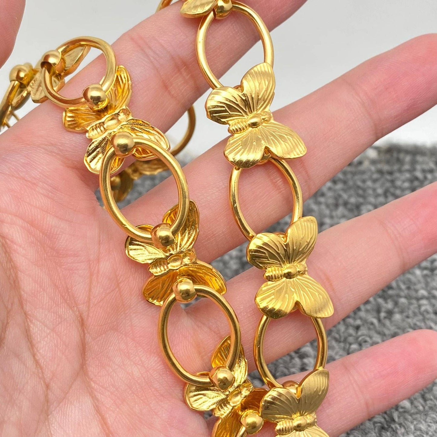 a hand holding a gold necklace with butterflies and circle links