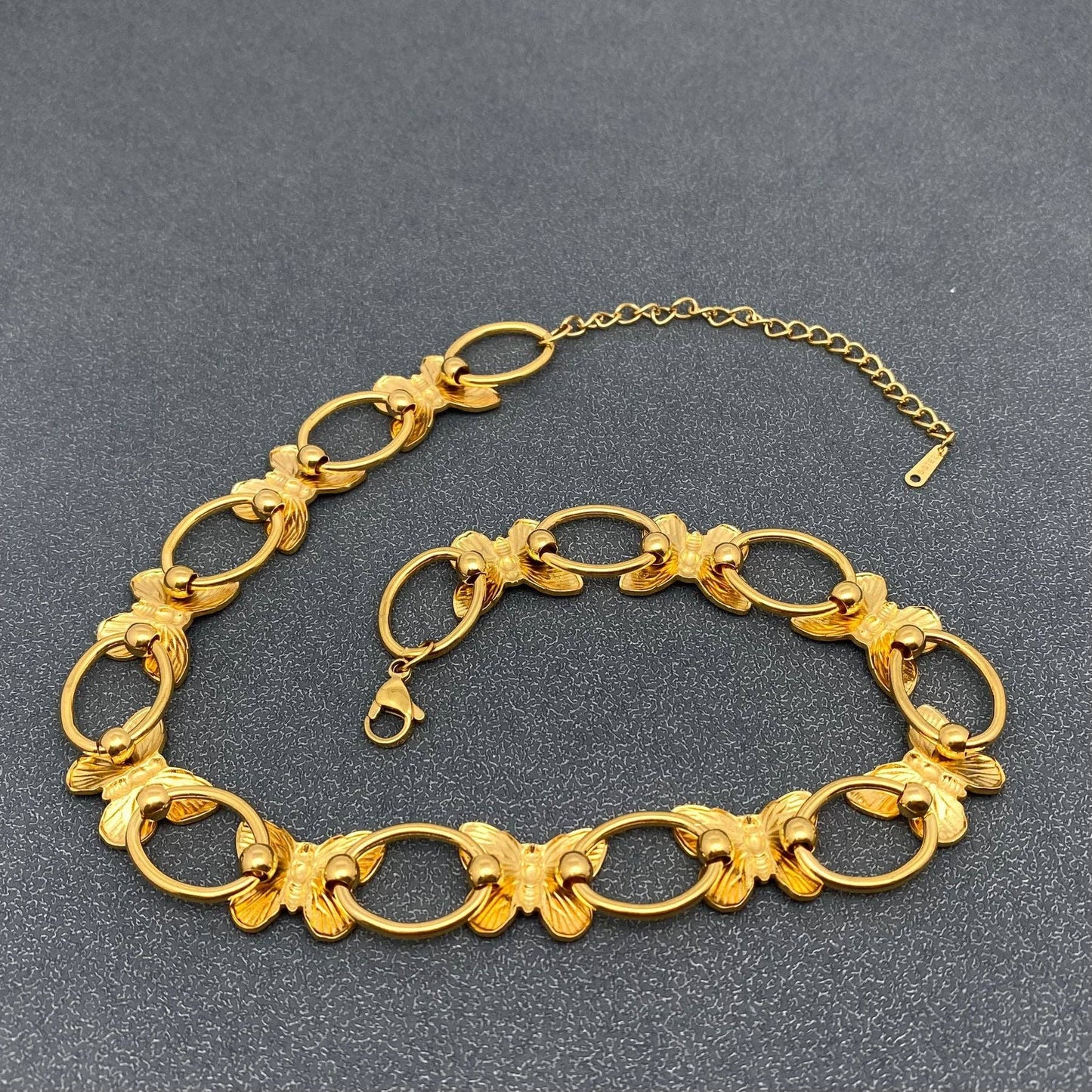 back view of a gold necklace with butterflies and circle links laying on a grey background