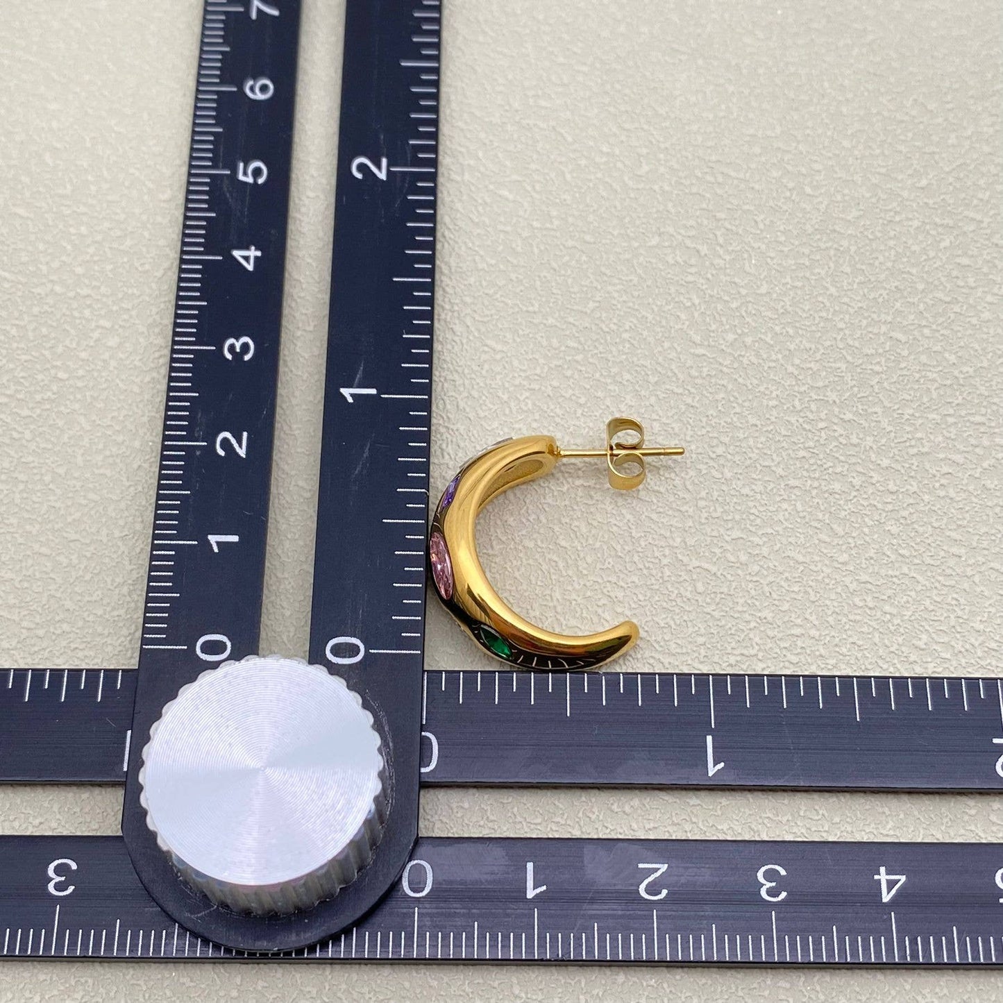 one gold multi color inlaid crystal earring next to a black rule on an ivory background
