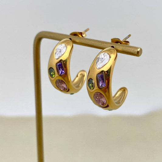 a pair of gold multi color crystal inlaid hoop earrings on gold stand