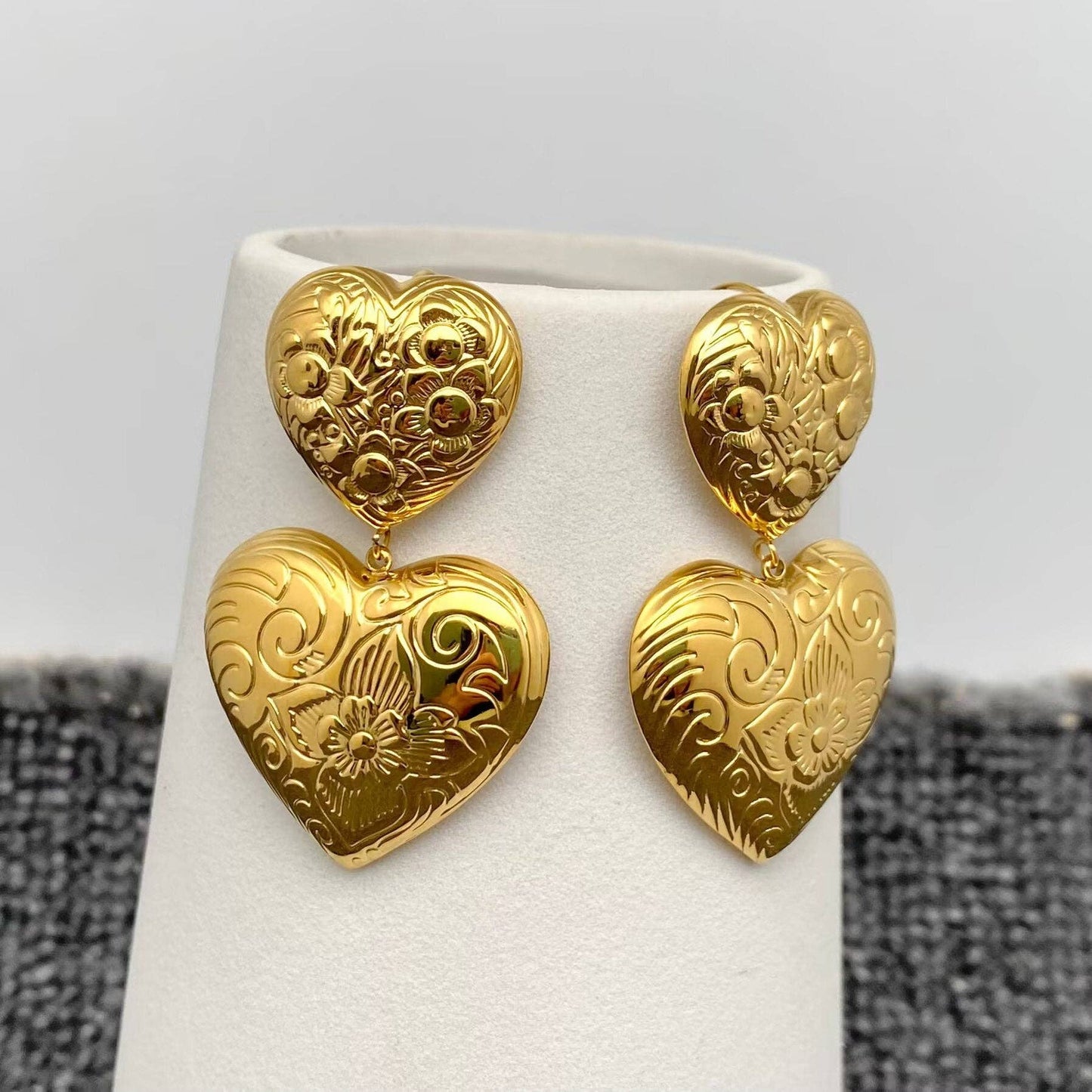 a pair of gold embossed double heart earrings hanging on a white vase