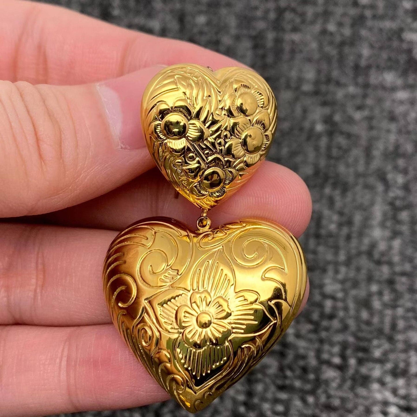 up close view of one gold embossed double heart earring in a hand