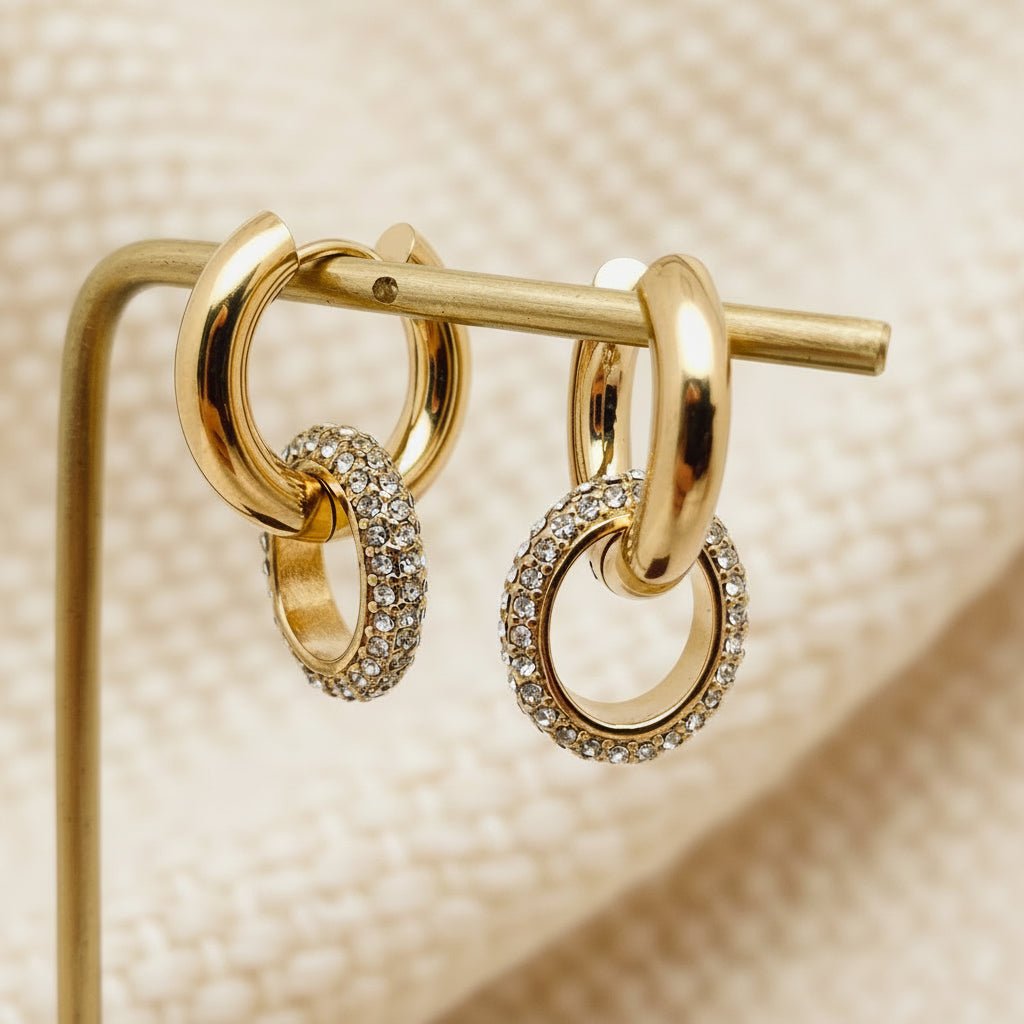 Gold hoop earrings with embedded stones on a stand against an ivory background