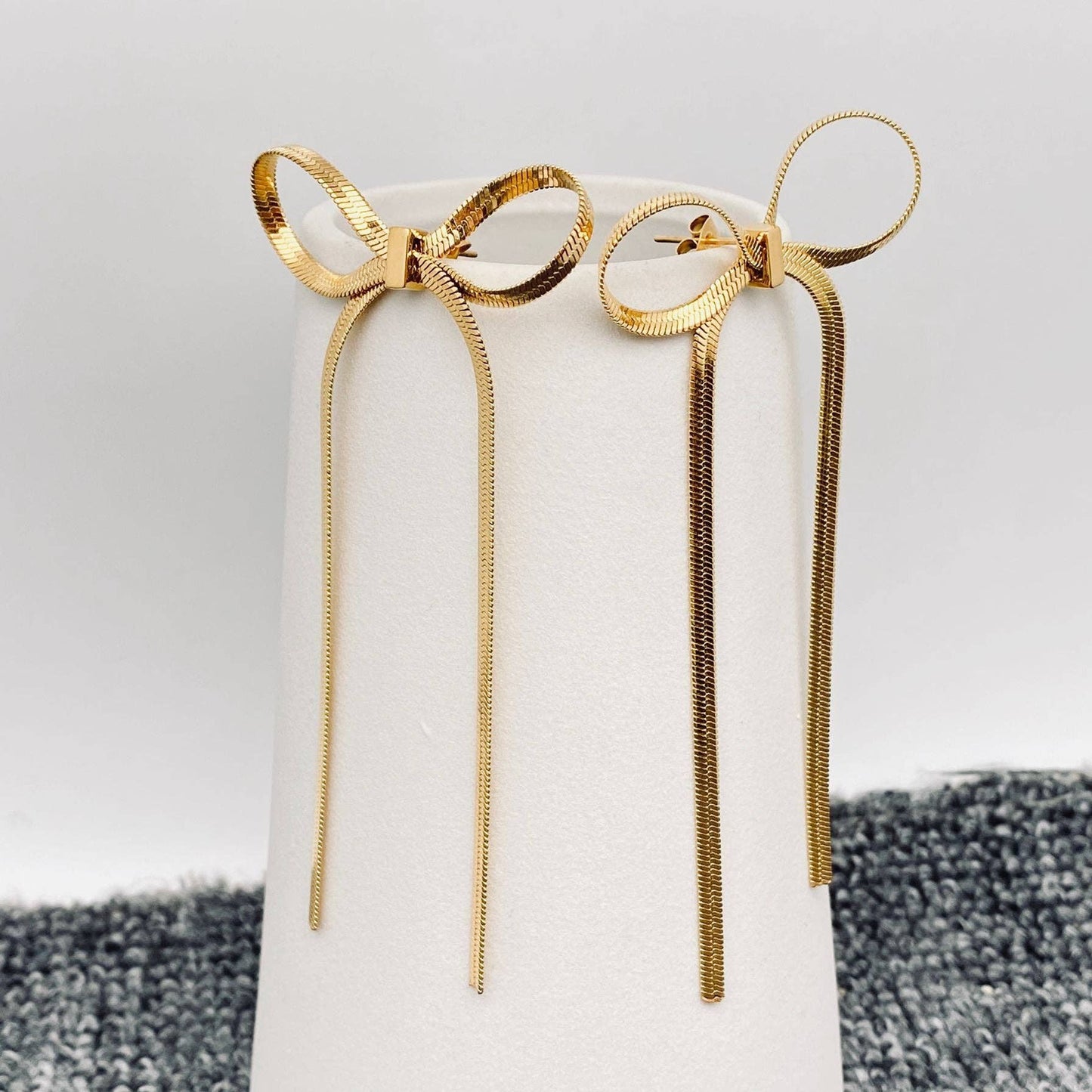 gold chain bow earrings on a white stand