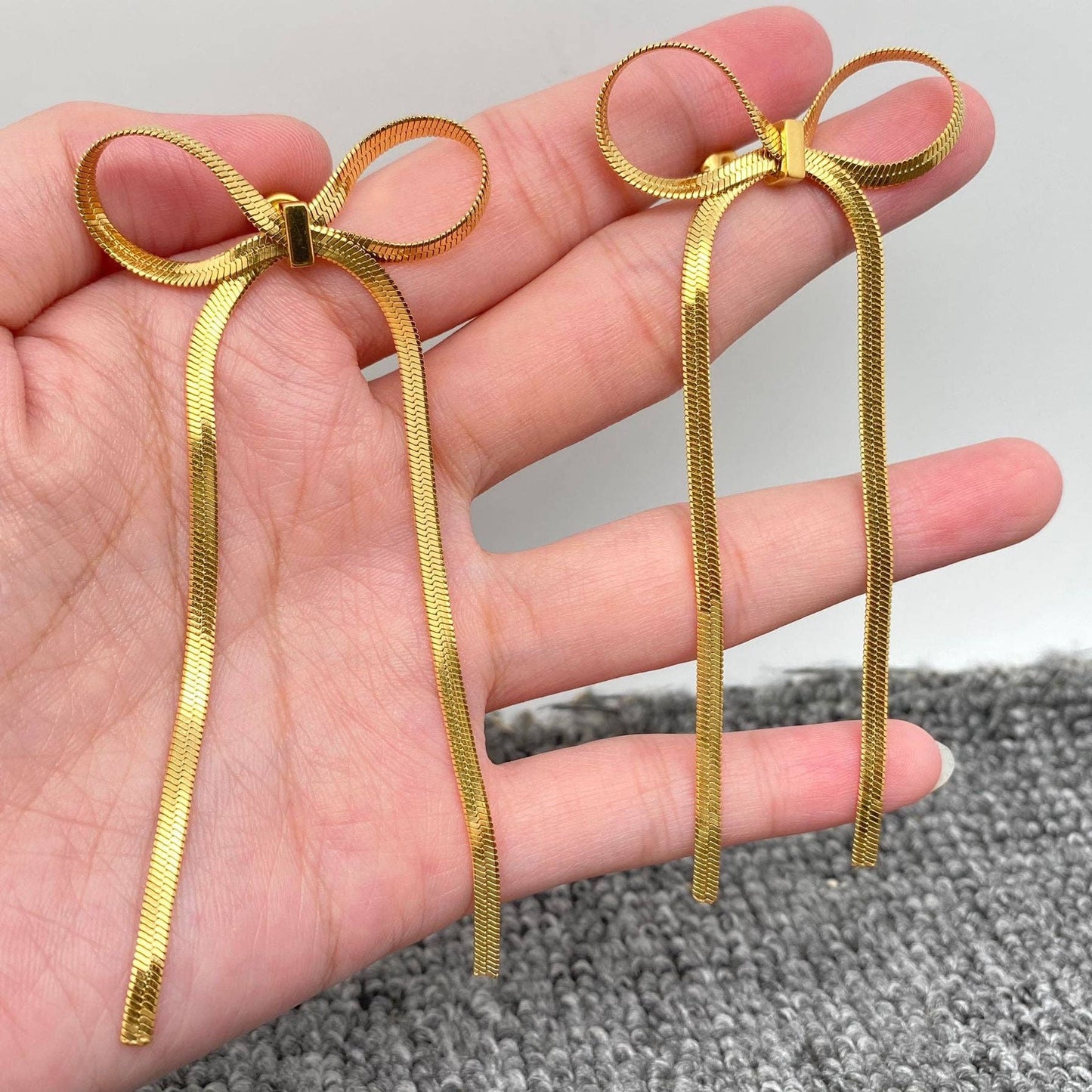 hand holding gold chain bow earrings